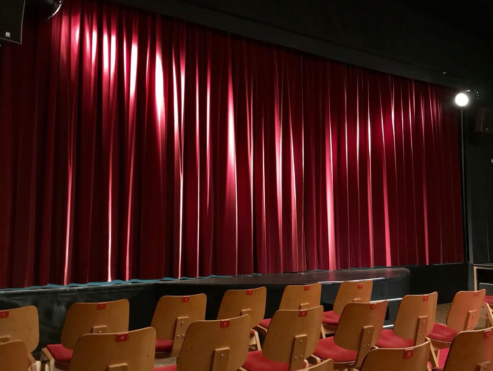 A grand theatre auditorium seen from the stage, red seats and gilded balconies