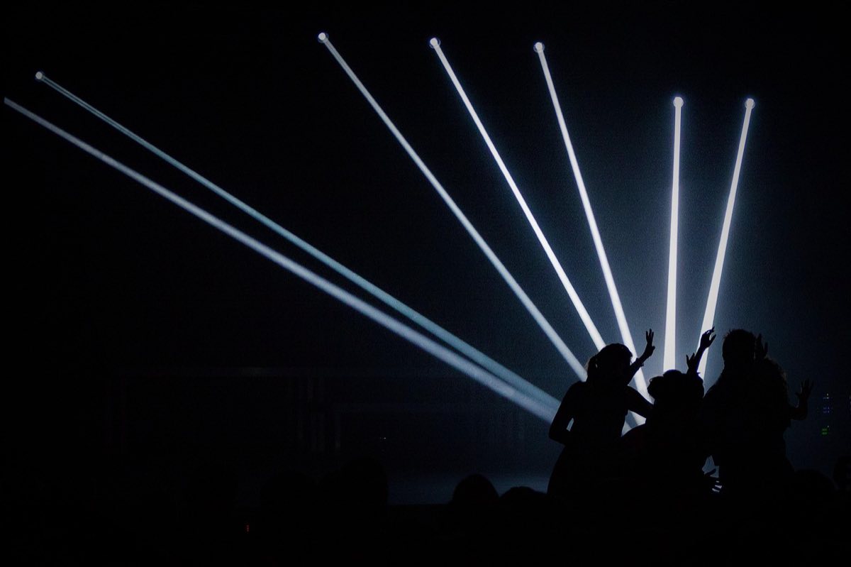 Performers silhouetted against beams of white stage light